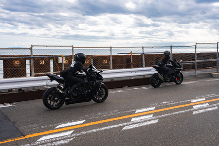 Motorcyclists ride Kamakura coastal road by numbered seawall and bay