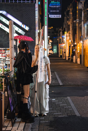 Street fashion chat in neon lit Tokyo alley near convenience storeの写真素材