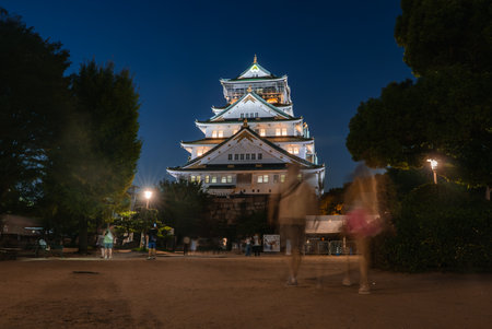 Osaka Castle illuminated at night with visitors on the approach pathの写真素材