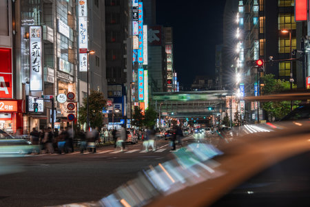 Night crowds cross neon intersection in Tokyo with motion blurの写真素材
