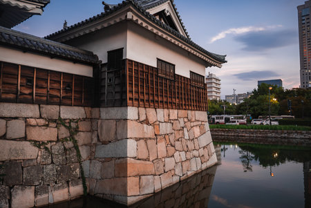 Osaka Castle turret and moat at dusk with city buildings across waterの写真素材