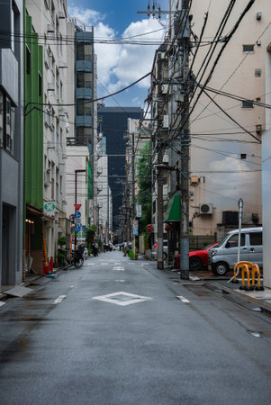 Tokyo side street with power lines, wet pavement, and storefrontsの写真素材