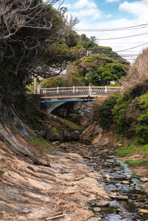 Rocky stream in a tree lined ravine leading to a small bridge in Kamakuraの写真素材