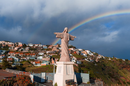 Cristo Rei statue at Garajau above Madeira coast under rainbowの写真素材