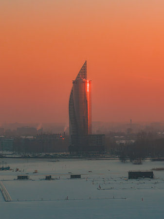 Sail like glass skyscraper at sunset over frozen riverside in Riga