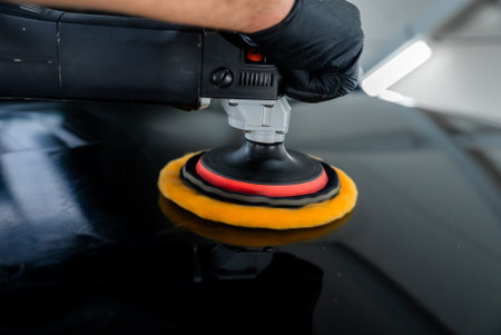 Detailer guides dual action polisher on glossy black car panel