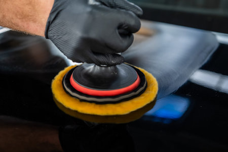 Detailer guides dual action polisher on glossy black car panel