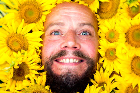 Close-up portrait of a bearded man in sunflower flowers.