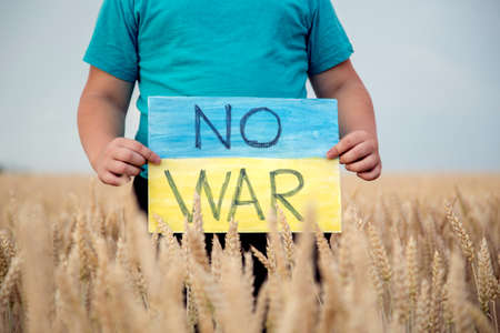 A child in a wheat field holds a banner against war. Ukrainian child against the war. Children's patriotism. Children who have no faces.の写真素材