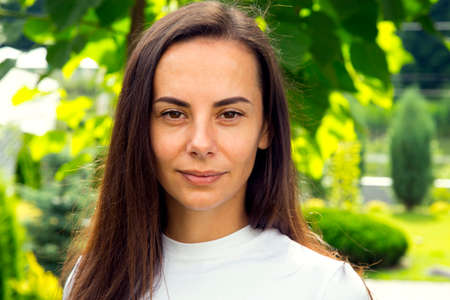 Portrait of a young beautiful woman in the park. The face of a happy girl who looks at the camera in...