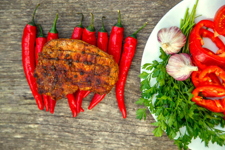 Meat steak cooked on the barbecue. Grilled fresh meat steak with spices and red pepper. Ready steak on the table with tomatoes and peppers. The concept of food, restaurants, traditionの写真素材