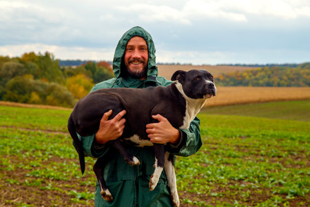 A man walks his dog in a field after a thunderstorm. Guy with staffordshire terrier in nature on a cloudy day. The concept of freedom, happiness, friendship, nature.の写真素材