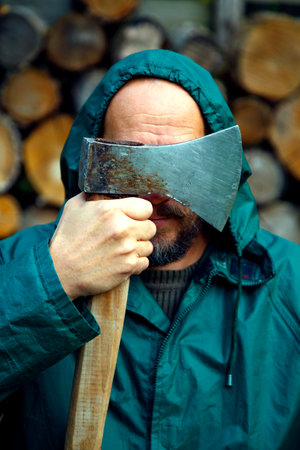 Portrait of a real bearded man with an axe. Bearded lumberjack with an ax in his hand. A man with an ax against the background of stacked firewood. The concept of strength, courageの写真素材