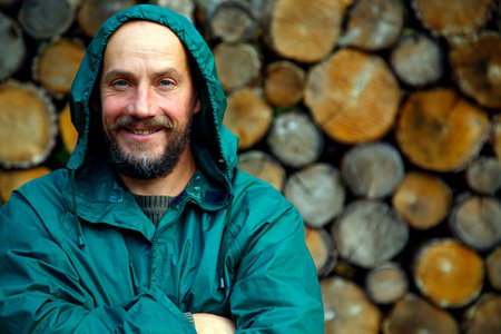 Portrait of a bearded man on a background of firewood. A bearded man poses for the camera after cutting firewood in the forest. The concept of masculinity, naturalism, survival.の写真素材