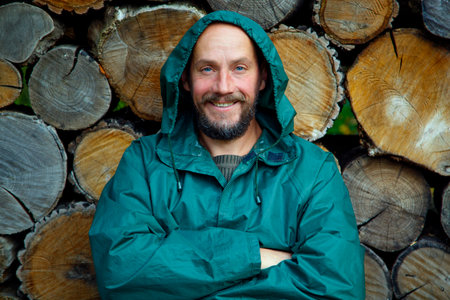 Portrait of a bearded man on a background of firewood. A bearded man poses for the camera after cutting firewood in the forest. The concept of masculinity, naturalism, survival.の写真素材
