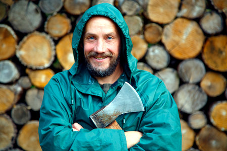 Portrait of a real bearded man with an axe. Bearded lumberjack with an ax in his hand. A man with an ax against the background of stacked firewood. The concept of strength, courageの写真素材