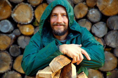 Portrait of a man with a bunch of chopped firewood. Bearded lumberjack with firewood for the fireplace. The concept of survival, recreation, country pastime.の写真素材