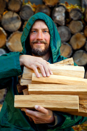 Portrait of a man with a bunch of chopped firewood. Bearded lumberjack with firewood for the fireplace. The concept of survival, recreation, country pastime.の写真素材