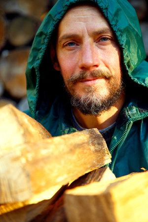 Portrait of a man with a bunch of chopped firewood. Bearded lumberjack with firewood for the fireplace. The concept of survival, recreation, country pastime.の写真素材