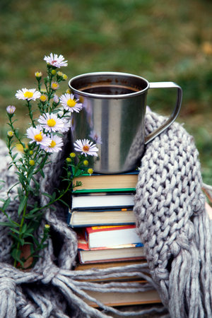 Cup of coffee with books and knitted scarf on the grass.A cup of coffee on a background of books and a blanket.の写真素材
