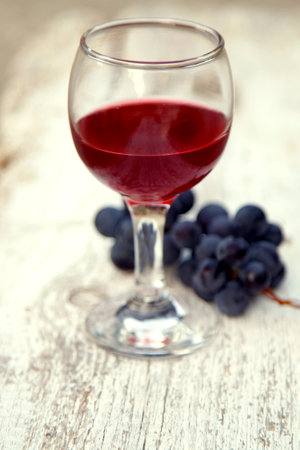 Glass with red wine and a bunch of grapes in the garden. Red wine in a glass and a bunch of grapes.の写真素材