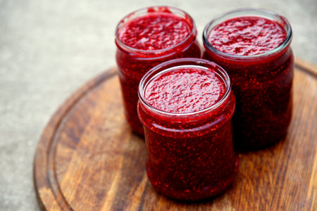 Homemade raspberry jam in glass jars on a wooden board, selective focus.Raspberry jam in canning...