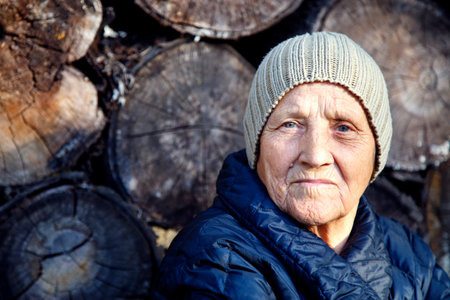 Portrait of an elderly woman against the background of old firewood. The face of an old woman in a...