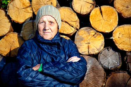 Portrait of an elderly woman against the background of old firewood. The face of an old woman in a...