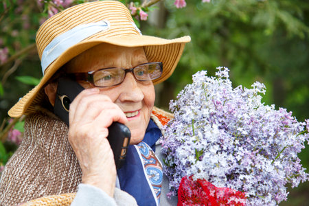 An old woman is talking on a mobile phone on a bench in a park. An elderly woman uses a mobile phone in the garden of a nursing home.の写真素材
