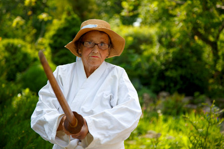 An old lady in a park with a sword. Portrait of an old lady training with a sword in the garden. The concept of old age, sports, nature.の写真素材