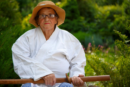 An old lady in a park with a sword. Portrait of an old lady with a sword in the garden. The concept of old age, sports, nature.の写真素材