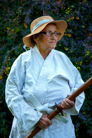 An old lady in a park with a katana. Portrait of an old lady training with a katana in the garden. The concept of old age, sports, nature.の写真素材