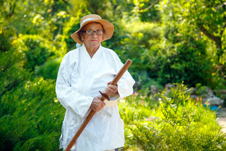 An old lady in a kimono in a park with a wooden stick. Portrait of an old lady training with a wooden stick in the garden. The concept of old age, sports, nature.の写真素材