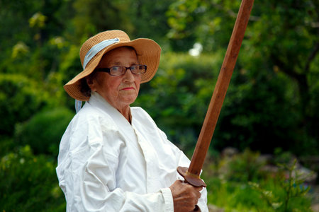 An old lady in a kimono in a park with a katana. Portrait of an old lady training with a katana in...