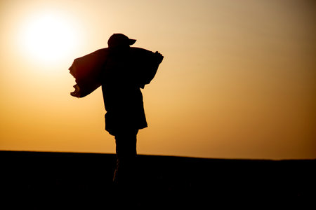 Silhouette of a male farmer with a sack of wheat on his shoulder. A male worker at sunset with a bag in his hand. The concept of farming, agriculture, hard work of workers.の写真素材