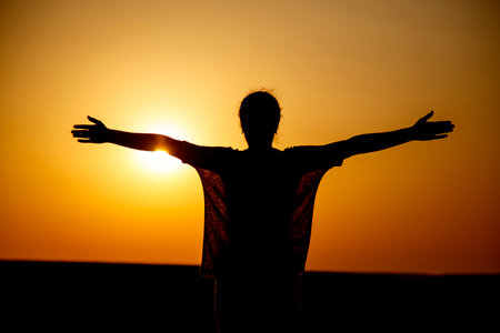 Portrait of a silhouette of a girl in a field showing figures with her hands. Silhouette of a young woman in a field at sunset.の写真素材