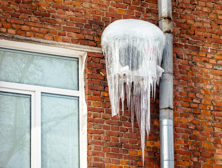 Air conditioner, covered with icicles on the brick wall of the house.