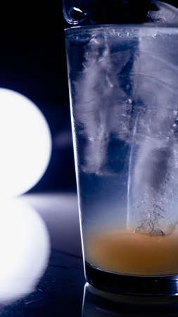 Glass with drink and ice, light spot on background