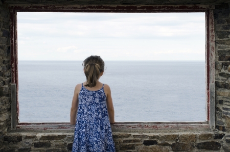 Lone little girl standing on window in front of the seaの写真素材