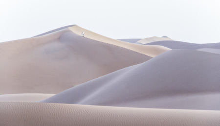A man climbing a dune in the desert of Chigaga, Moroccoの写真素材