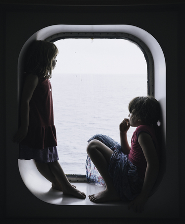 Two little girls looking the sea from a cruise windowの写真素材