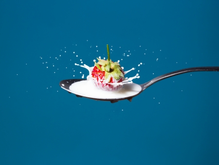 High-speed photo of strawberry falling into the milk on a blue backgroundの写真素材