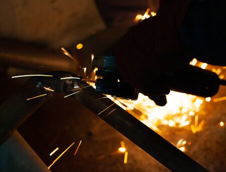 A worker with a cutting machine saws a pipe in a dark room