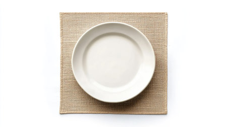 A simple white plate sits elegantly on a textured beige placemat, showcasing a minimalist and modern table setting perfect for dining and decor inspiration.の素材