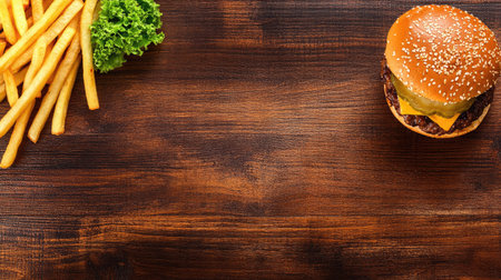 Top view of a classic cheeseburger with fries on a wooden table. Copy space available.の素材