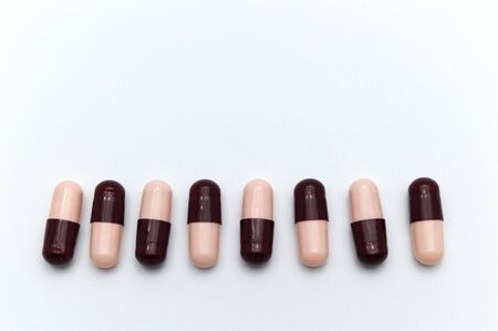 Prescription drugs, capsules of soft pink and dark reddish brown colors all mixed in. On white background.の写真素材