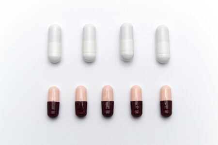 Prescription drugs, capsules of different colors between white capsules and dark reddish brown and soft pink all mix in . On white background.の写真素材