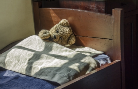 Old teddy bear lying in antique bedの写真素材