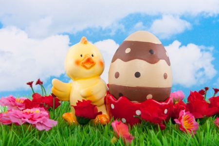a chick egg shell with an easter egg on a green lawn with flowers against a blue cloudy skyの写真素材