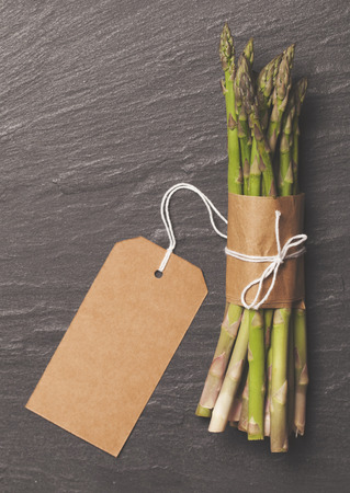 Fresh asparagus tied in a bunch on a rustic slate background with blank tagの写真素材